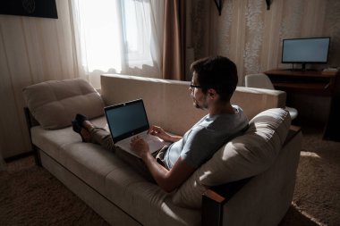 Uzaktan kumanda. Dizüstü bilgisayarda çalışan bir adam evdeki koltukta oturuyor. Metin için Boşluğu Kopyala. Serbest çalışan hipster, ortaklarıyla çalışır, çalışır ya da iletişim kurar.