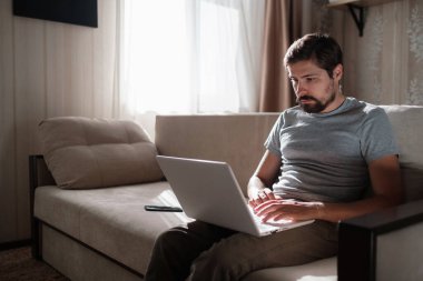 Uzaktan kumanda. Dizüstü bilgisayarda çalışan bir adam evdeki koltukta oturuyor. Metin için Boşluğu Kopyala. Serbest çalışan hipster, ortaklarıyla çalışır, çalışır ya da iletişim kurar.