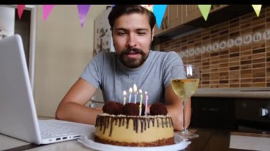 Adam doğum günü pastasının mumunu üflüyor ve video görüşmesi yapıyor. Karantina zamanında doğum gününü kutlayan adam.