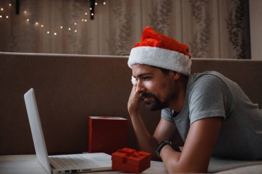 Noel zamanı evdeki kanepede oturan kırmızı bardaklı hippi bir adam. Sanal Noel partisi. Çevrimiçi takım toplantı video konferansı evden arıyor..