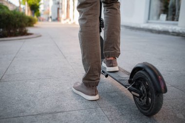 Gün batımında şehir manzarasında siyah elektrikli scooter kullanan adama yakın çekim. Elektrik kentsel ulaşım konsepti resmi