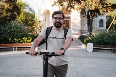 Şehrin arka planında scooter süren çekici bir adam. Şehirde elektrikli scooter sürmek eğlenceli..