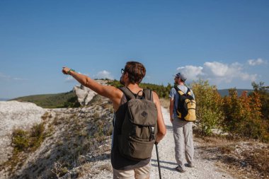 Sırt çantalı iki yürüyüşçü ve diğer tırmanma ekipmanları Rock 'ın tepesinde kalıyor. Adam eliyle güzergahı işaret ediyor. Plan, vizyon ve görev konsepti.