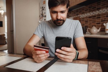 Hipster genç adam evde akıllı telefon kullanarak online alışveriş yapıyor. Kapalı alanda. çevrimiçi alışveriş kavramı.