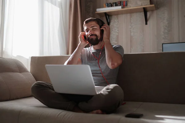 Man on sofa with headphones and notebook at home. young hipster wear headphones study online watching webinar podcast on laptop listening learning education course or music, elearning concept