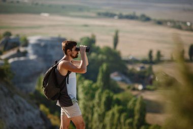 Tepedeki dürbüne bakan adam. Sırt çantalı bir adam. Vadi manzarasında yürüyüş yapan genç beyaz bir adam.