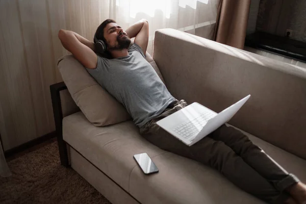 Man on sofa with headphones and notebook at home. young hipster wear headphones study online watching webinar podcast on laptop listening learning education course or music, elearning concept