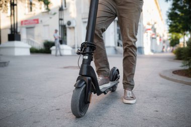 Gün batımında şehir manzarasında siyah elektrikli scooter kullanan adama yakın çekim. Elektrik kentsel ulaşım konsepti resmi