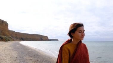 Sahildeki kadın. Sarı kazaklı genç mutlu kadın deniz kıyısında yürüyor. Deniz dalgalarına bakıyor..