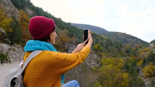 スマートフォンを使用してバックパックを持つ女性 山の中でハイキングやスマートフォンで写真を撮る スマートフォンを使用してソロ女性ハイカー 女性ハイカーは山のスマートフォンの写真を撮る — ストック動画