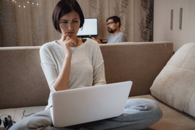Yoğun bir adam ve kadın evdeki oturma odasında laptopla sıkı çalışıyor. Kendi kendini yalıtırken ev ofisi, 2019