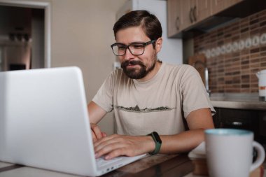 Gözlük takan, dizüstü bilgisayar kullanan, klavyeye yazan, e-posta ya da mesaj yazan, sohbet eden, alışveriş yapan, bilgisayar üzerinde çalışan, mutfakta oturan başarılı bir serbest çalışan genç adam.