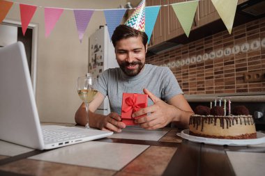 Karantina zamanında doğum gününü kutlayan bir adam. Coronavirus salgını 2020. Adam kutuyu açıyor ve hediyeyle çok mutlu oluyor. Arkadaşlarla uzaktan iletişim kurmak.