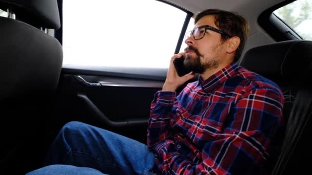Uśmiechnięty brodaty biały mężczyzna w koszuli w kratę siedzi na siedzeniu pasażera i rozmawia przez telefon. — Wideo stockowe
