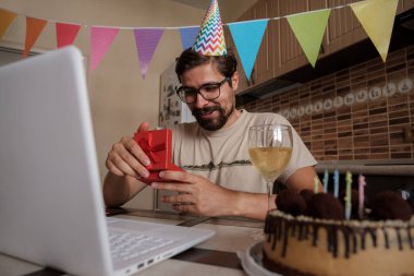 Karantina zamanında doğum gününü kutlayan bir adam. Coronavirus salgını 2020. Adam kutuyu açıyor ve hediyeyle çok mutlu oluyor. Arkadaşlarla uzaktan iletişim kurmak.