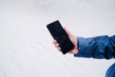 Kış mevsiminde, karla kaplı bir ormanda, bir adamın elinde güzel bir cep telefonu.