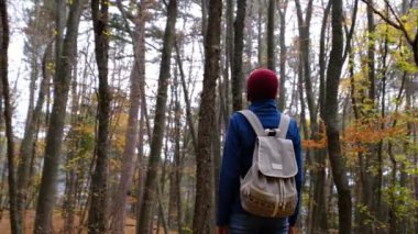 Sırt çantalı bir kadın ormanda yolda yürüyor..