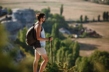 Sırt çantasıyla doğa yürüyüşü yapan adam portresi. Beyaz adam yaz gezisinde arka planda vadiyle mutlu bir şekilde gülümsüyor..