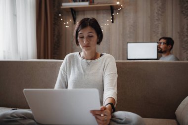 Yoğun bir adam ve kadın evdeki oturma odasında laptopla sıkı çalışıyor. Kendi kendini yalıtırken ev ofisi, 2019