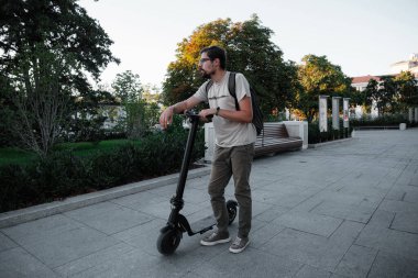 Şehrin arka planında scooter süren çekici bir adam. Şehirde elektrikli scooter sürmek eğlenceli..