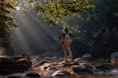 Bir kadın doğayla çevrili yeni, büyülü ve fantastik yerleri keşfeder ve nefes almak ve rahatlamak için kollarını açar. Dişi yürüyüşçü orman deresini geçiyor..