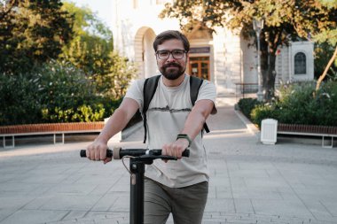 Şehrin arka planında scooter süren çekici bir adam. Şehirde elektrikli scooter sürmek eğlenceli..