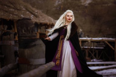 Kalenin zeminine karşı siyah pelerin giymiş güzel sarışın Viking. Güzel bir film seti. Eski bir Viking köyü.