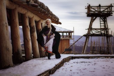 Kalenin zeminine karşı siyah pelerin giymiş güzel sarışın Viking. Güzel bir film seti. Eski bir Viking köyü.