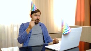 Gülümseyen, külahta şapkalı genç bir erkek online görüntülü sohbet kullanarak arkadaşını doğum günüyle kutluyor.