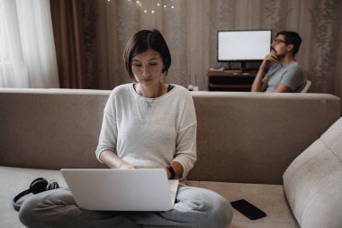 Yoğun bir adam ve kadın evdeki oturma odasında laptopla sıkı çalışıyor. Kendi kendini yalıtırken ev ofisi, 2019