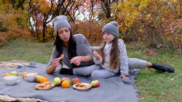 Feliz joven madre y dulce hija disfrutando de té y galletas en el parque. — Vídeos de Stock