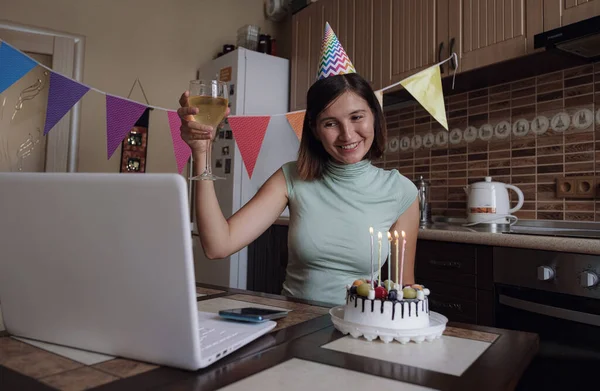 Woman blowing out the candle on the birthday cake and making video call. Lady celebrating birthday online in quarantine time. Authentic decorated home workplace. Coronavirus outbreak 2020.