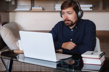 Mutlu erkek öğrenci internet öğretmeni kulaklık takıyor, konuşma videosu çekiyor, dizüstü bilgisayar ekranına bakıyor, konferans sohbeti yapıyor Skype hocası ile iletişim kuruyor, uzaktan eğitim ve evde öğrenim kursları veriyor.