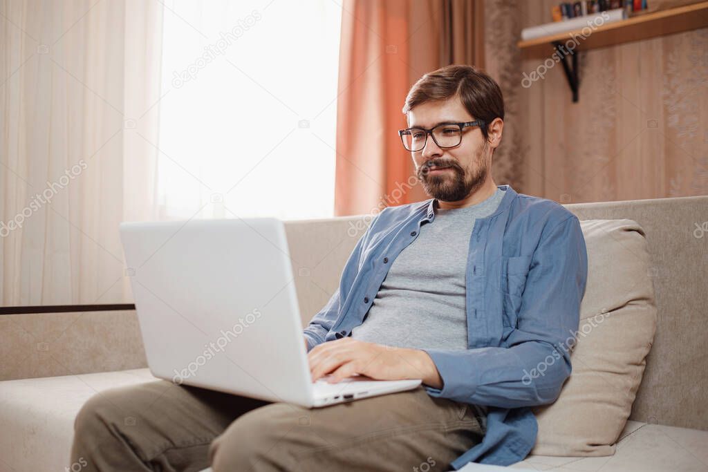 Handsome young man using laptop computer at home. Student men in his room. Online shopping, home work, freelance, online learning, studying concept. Distance education