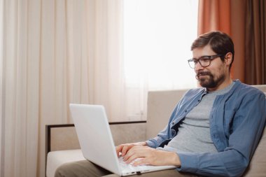 Evde dizüstü bilgisayar kullanan yakışıklı bir genç. Öğrenci erkekler odasında. Çevrimiçi alışveriş, ev işi, serbest çalışma, çevrimiçi öğrenme, öğrenim kavramı. Uzaklık eğitimi