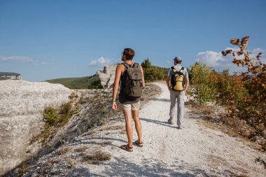 İki adam kayalık yamaçlarda yürüyüş çubuklarını kullanarak sırt çantalarını taşıyorlar. Dağlar Vadisi, insanların yanı sıra manzaralı. Doğaya yaz yolculuğu