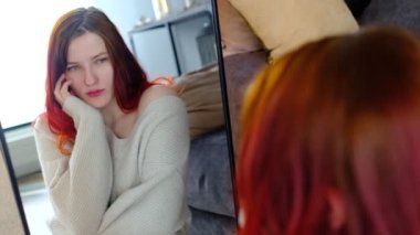 Kanepenin yanında oturan, poz veren, kameraya gülümseyen güzel, genç ve zarif bir kadın. Rahat bir daire ya da otel odası..