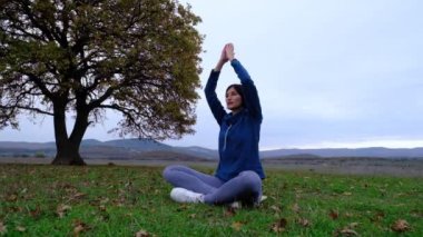 Kadınlar yalnız meşe ağacının yanındaki sonbahar parkında yoga yapmayı severler.