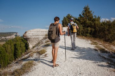 İki adam kayalık yamaçlarda yürüyüş çubuklarını kullanarak sırt çantalarını taşıyorlar. Dağlar Vadisi, insanların yanı sıra manzaralı. Doğaya yaz seyahati. Arka planda yürüyüşçü.