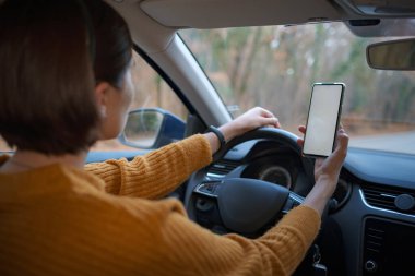 Sürücü araba kullanırken cep telefonunu boş ekran ile tutan ve kullanan bir kadının görüntüsü. İnsan, Sürücü, Navigasyon ve Ulaşım Konseptleri