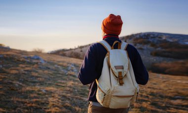 Bahar dağlarının tepesinde gün batımında duran ve doğanın tadını çıkaran genç bir adam. Dağ ve kıyı yolculuğu, özgürlük ve aktif yaşam tarzı
