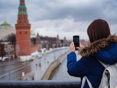 Genç Asyalı güzel turist Moskova Kremlin, Rusya 'nın arka planında cep telefonuyla fotoğraf çekiyor.