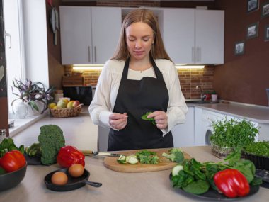 Sağlıklı yemek pişirirken mutfakta duran mutlu, genç bir sarışın bayan. Sağlıklı Yaşam Tarzı Konsepti. Evde yemek pişirmek. Yemek yapmak için sebze doğrama