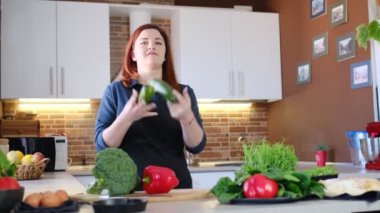 Ev yemeği ve evde yemek pişirme deneyimi konsepti. Kırmızı saçlı kadın mutfakta kabak hokkabazlığı yaparken taze sebzelerle sağlıklı kahvaltı hazırlıyor.