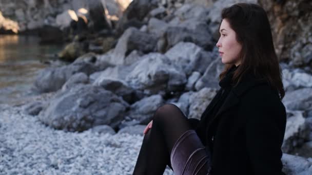 一位年轻美丽的亚洲女人 身穿黑色外套 穿着岩石 住在海滨 布鲁内特的女人喜欢海边的孤寂 — 图库视频影像
