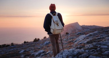 Bahar dağlarının tepesinde gün batımında duran ve doğanın tadını çıkaran genç bir adam. Dağ ve kıyı yolculuğu, özgürlük ve aktif yaşam tarzı