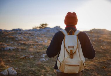 Bahar dağlarının tepesinde gün batımında duran ve doğanın tadını çıkaran genç bir adam. Dağ ve kıyı yolculuğu, özgürlük ve aktif yaşam tarzı