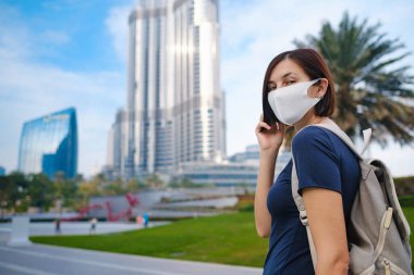 Dubai 'de arka planda gökdelenlerle dolaşan virüsü önlemek için maske takan güzel bir kadının portresi. Birleşik Arap Emirlikleri 'nde keyifli yolculuklar..