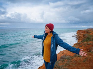 Sırt çantalı, sarı kazaklı ve kırmızı şapkalı hippi bir gezgin sahilde rüzgarın tadını çıkarıyor. Denizin üzerinde fırtına ve fırtınalar, seyahat ve keşfin mutluluk ve özgürlüğü.