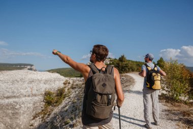 Sırt çantalı iki yürüyüşçü ve diğer tırmanma ekipmanları Rock 'ın tepesinde kalıyor. Adam eliyle güzergahı işaret ediyor. Plan, vizyon ve görev konsepti.